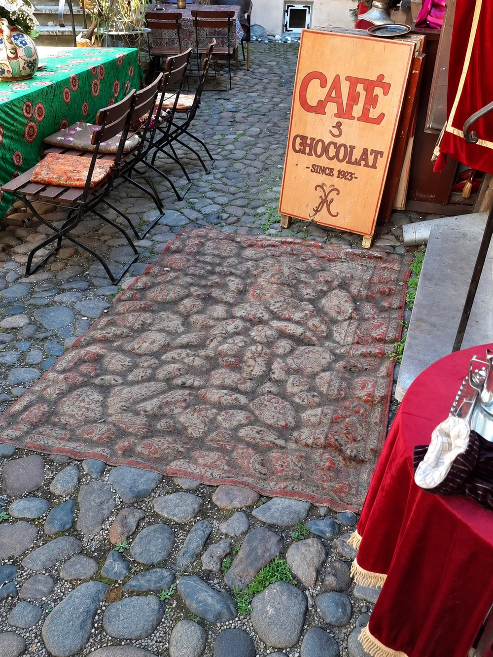 A patterned cafe rug pressed into the contours of an uneven cobblestone patio.