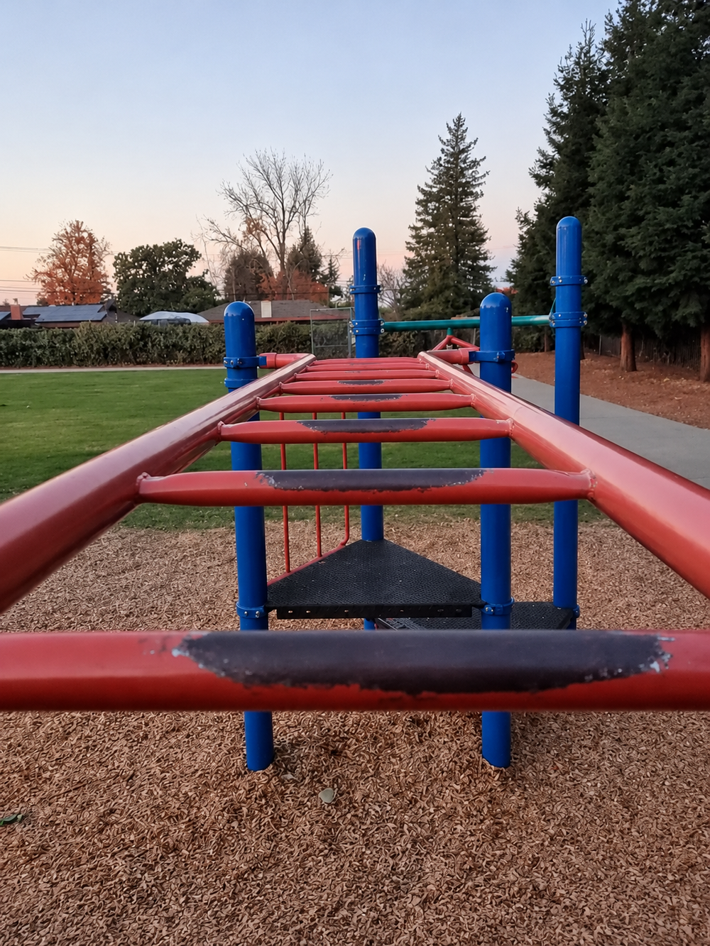 Red monkey bars with the paint worn away where children repeatedly grip the rungs.