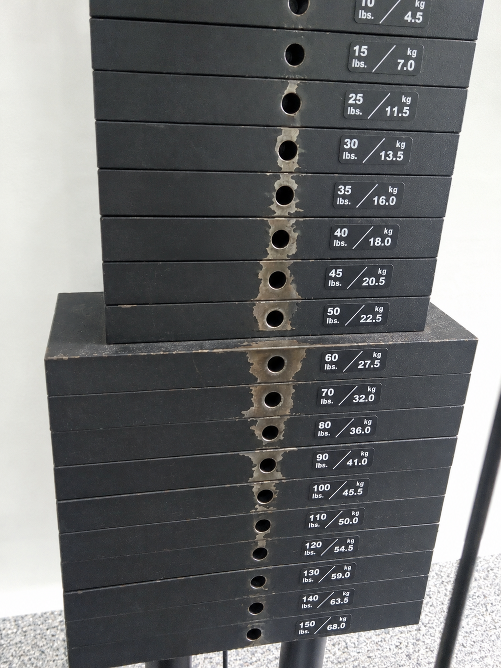 A gym weight stack with worn rings around the selector pin openings.
