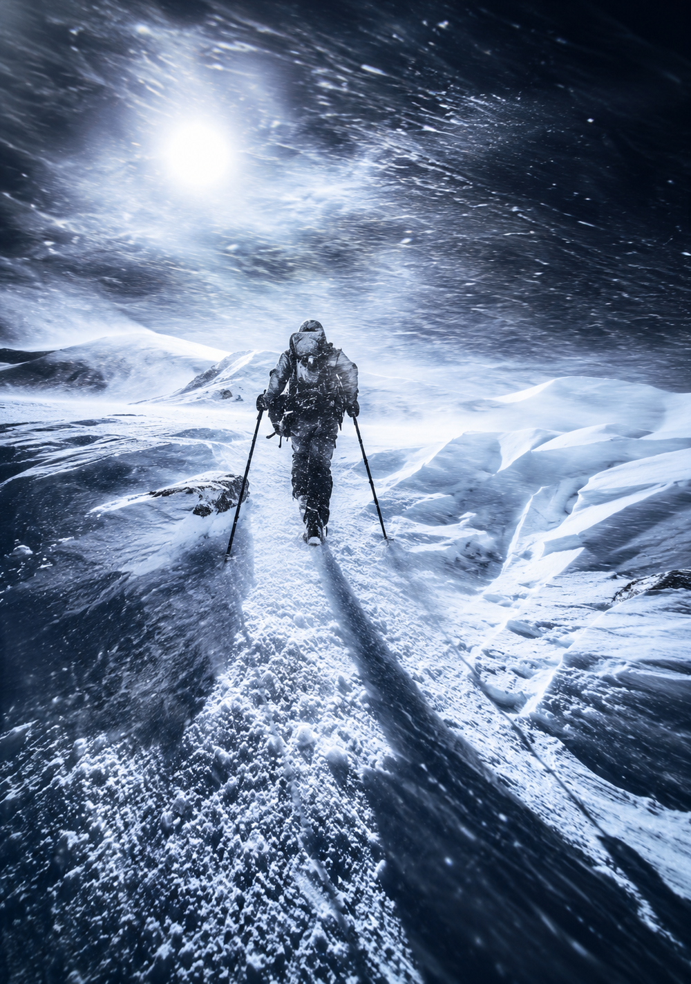 A climber wearing winter gear treks through a heavy snowstorm on a mountain ridge.
