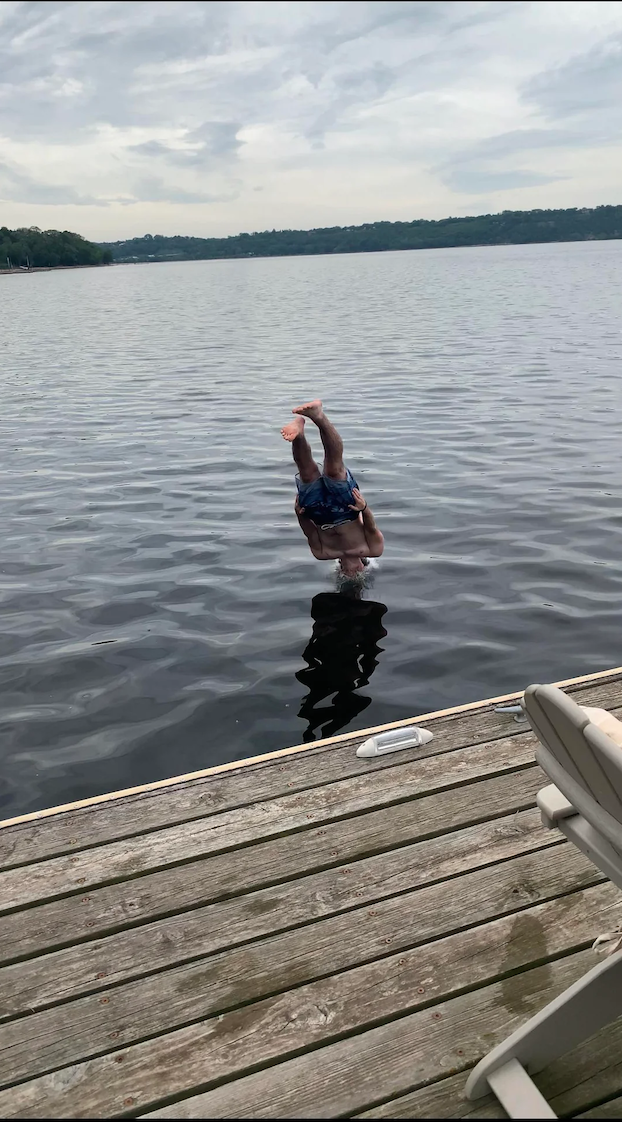 A person diving headfirst into a lake from a wooden dock.