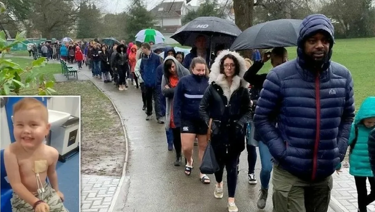 A long line of people in rain gear walking along a park path, with an inset photo of a young boy with medical patches on his chest.