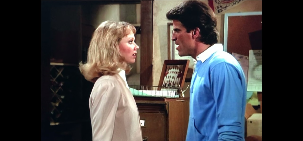 A man and a woman in an office facing each other in conversation.
