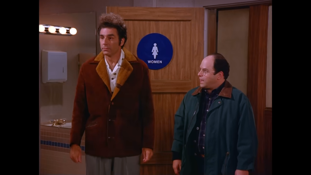 Cosmo Kramer and George Costanza standing in front of a women’s restroom door.