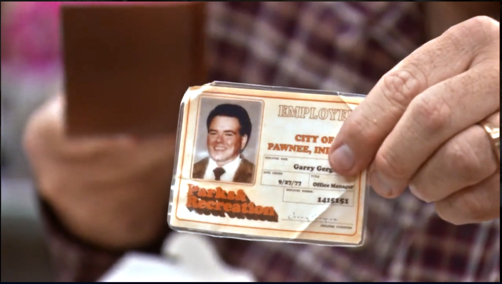 A hand holds a City of Pawnee employee ID badge for Garry Gergich, Office Manager.