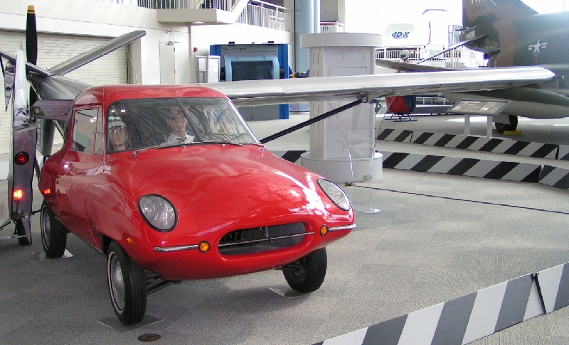 A red Aerocar flying car prototype with folded wings on display inside a museum.