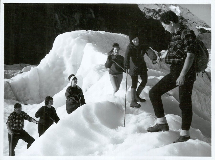 A group of five people hike across a snowy, mountainous terrain.