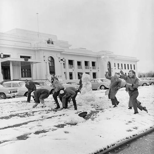 A group of people throwing snowballs in front of a large public building.