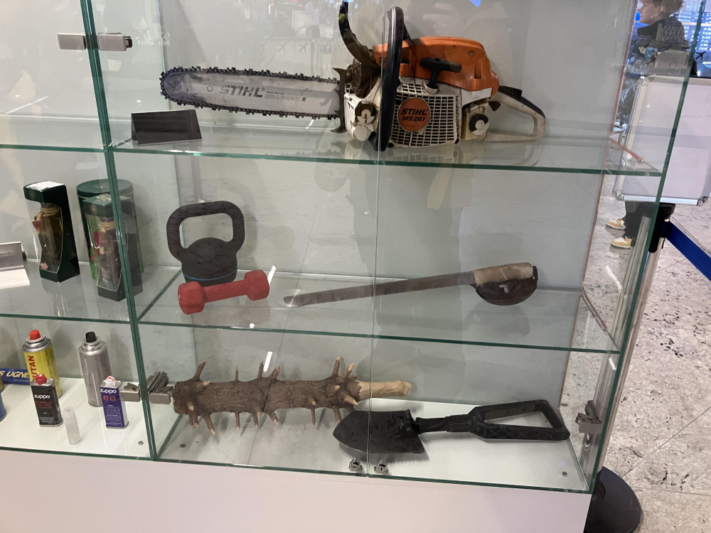 A display case containing a Stihl chainsaw, a kettlebell, a dumbbell, a machete, a spiked wooden club, a shovel, and small fuel containers.