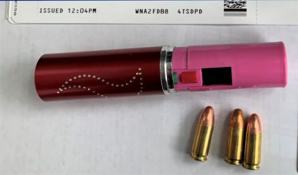 A red and pink cylindrical object resembling lipstick next to three brass cartridges on a white surface with a printed label above.