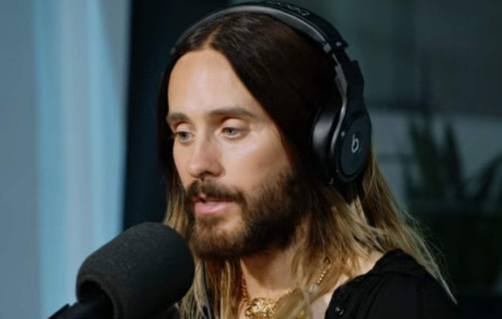 Jared Leto wearing black Beats headphones and speaking into a microphone.