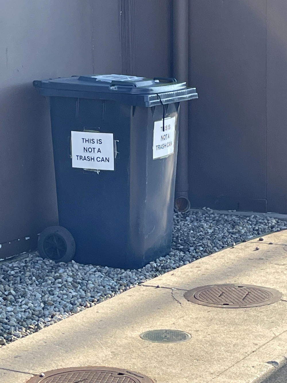 A dark blue rolling bin with signs on the front and side that read “This is not a trash can.”