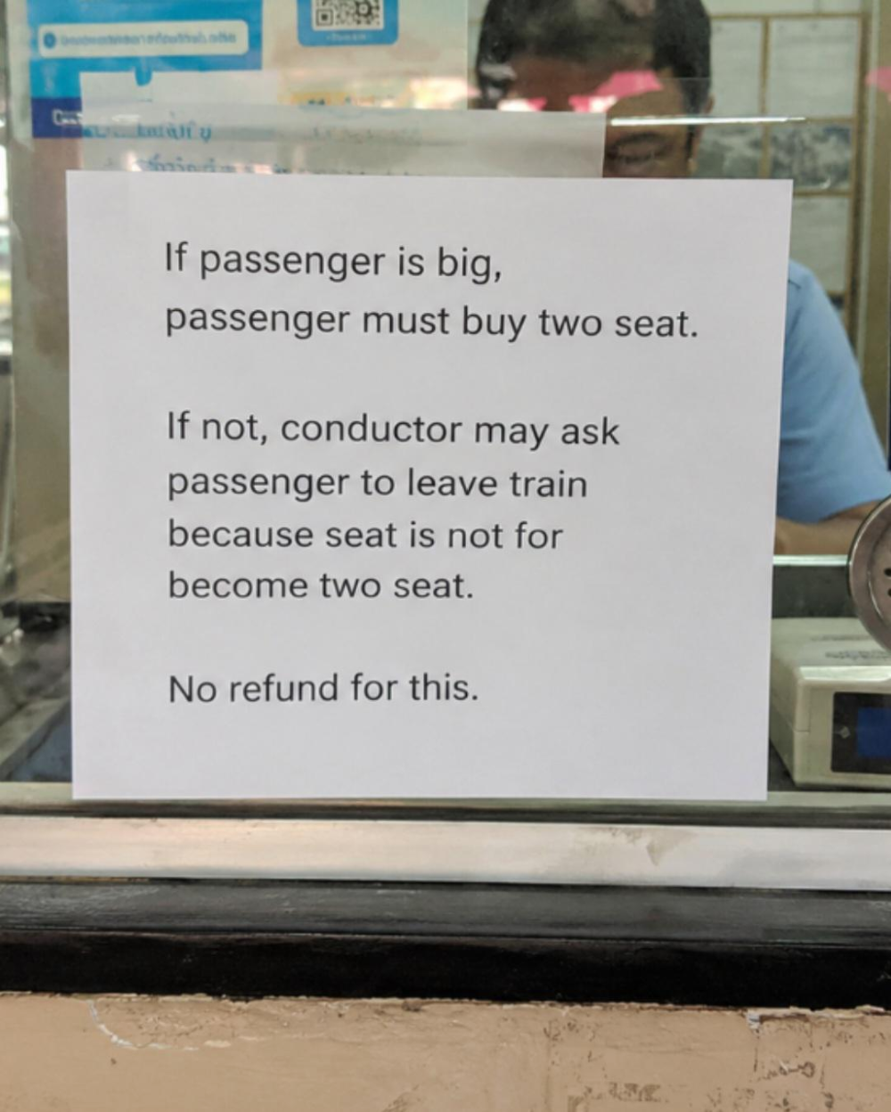 A sign posted on a window stating that large passengers must purchase two seats or risk being asked to leave the train without a refund.