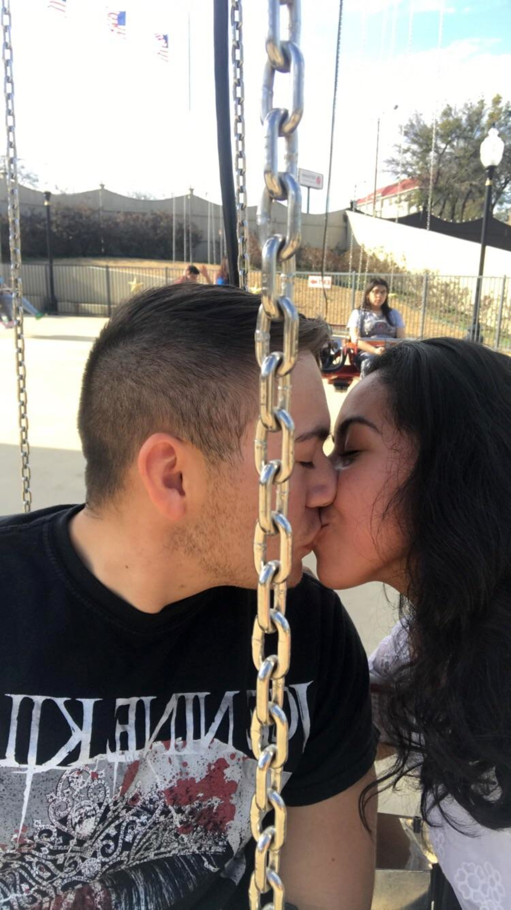 A couple kissing while sitting on a swing ride.