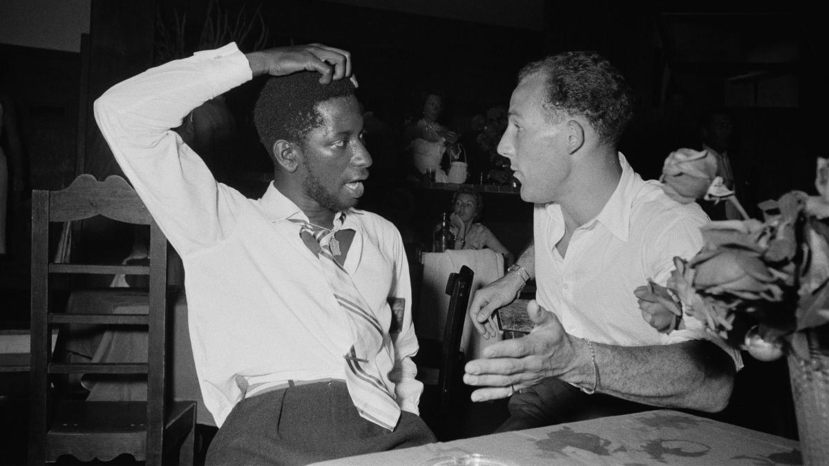 Two men in white shirts sitting at a table engaged in conversation.