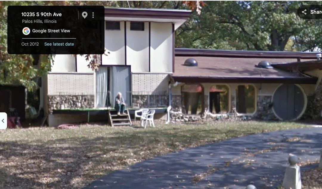 A person sits on the deck of a mid-century style house with stone masonry and circular windows.