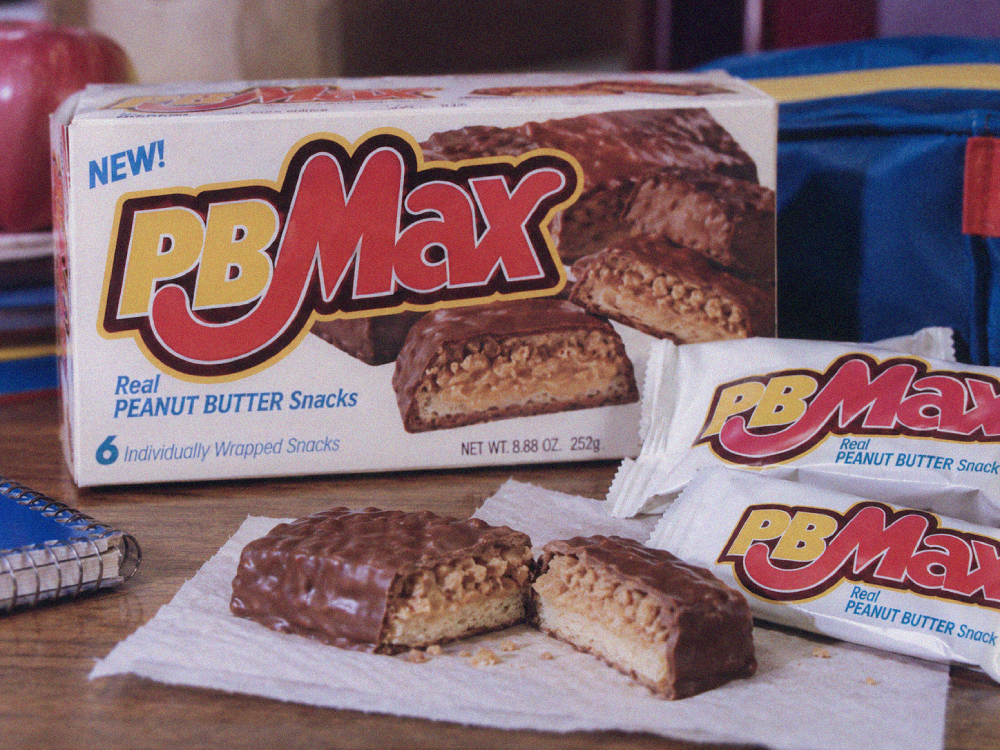 A box of PB Max peanut butter snacks with two individually wrapped bars and one snack broken in half on a piece of paper.