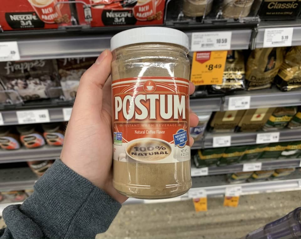 A hand holds a jar of Postum instant warm beverage in a grocery store aisle.