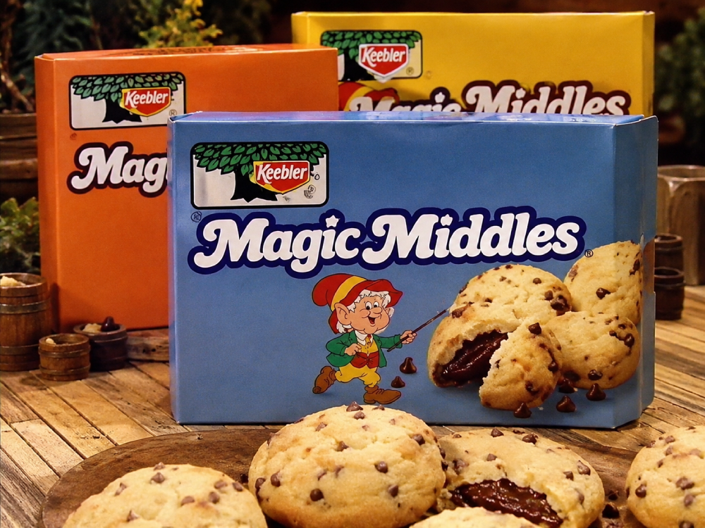 Three boxes of Keebler Magic Middles cookies sitting on a wooden surface, with loose chocolate chip cookies in the foreground.