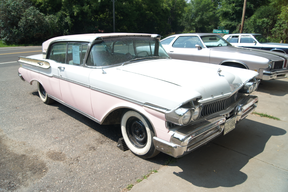 A vintage white and pink Mercury Turnpike Cruiser parked on the side of a road.