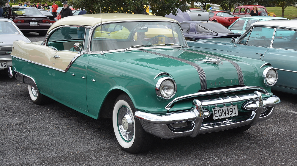 A vintage two-tone teal and cream Pontiac parked at a car show, with a chrome hood ornament and license plate EGN491.