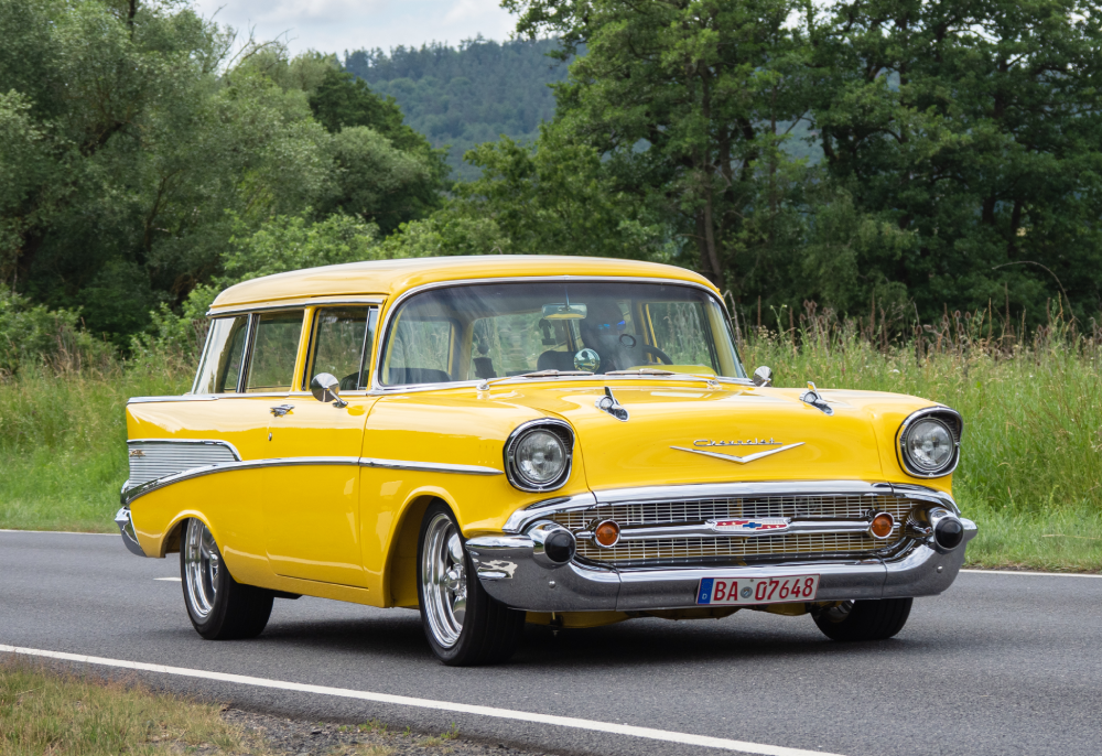 Bright yellow vintage Chevrolet station wagon driving on a country road.