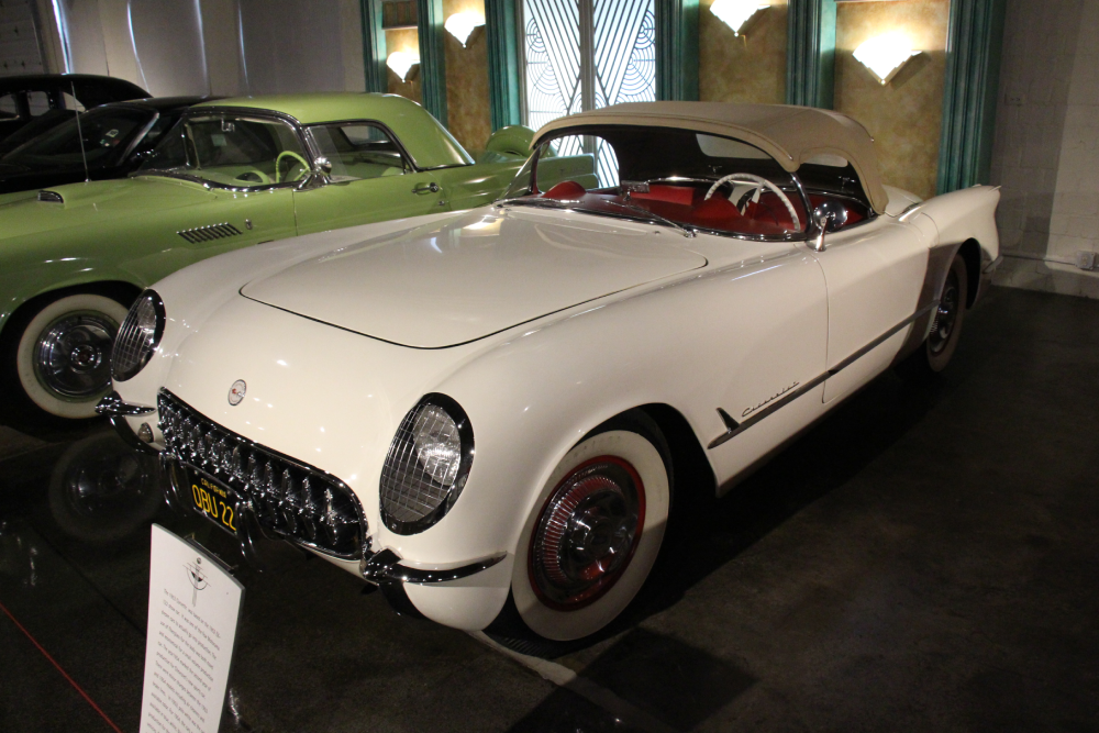 A white vintage Chevrolet Corvette convertible with a red interior parked next to a light green vintage car.