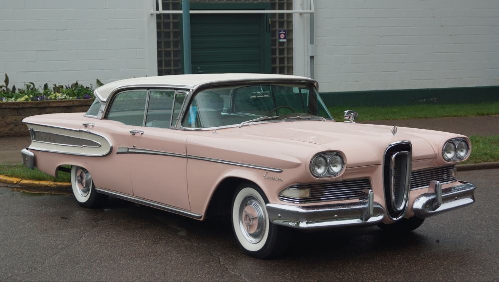 A vintage pink and white Edsel sedan parked on an asphalt surface.