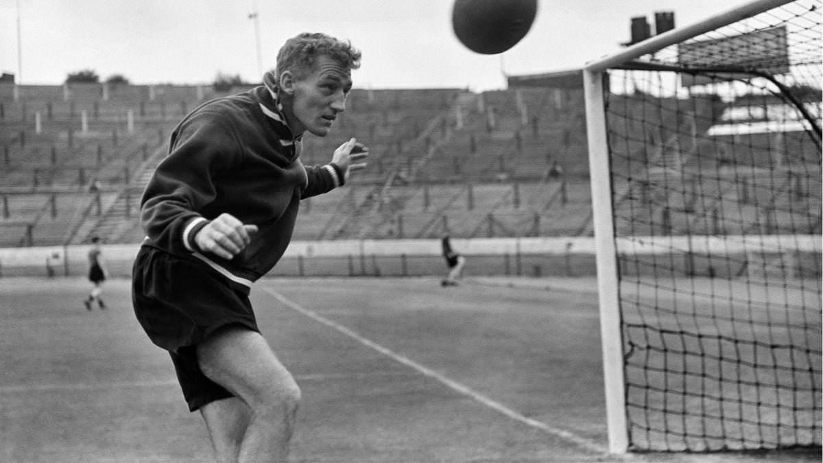 A soccer player prepares to head a ball in front of a goal net on a stadium field.