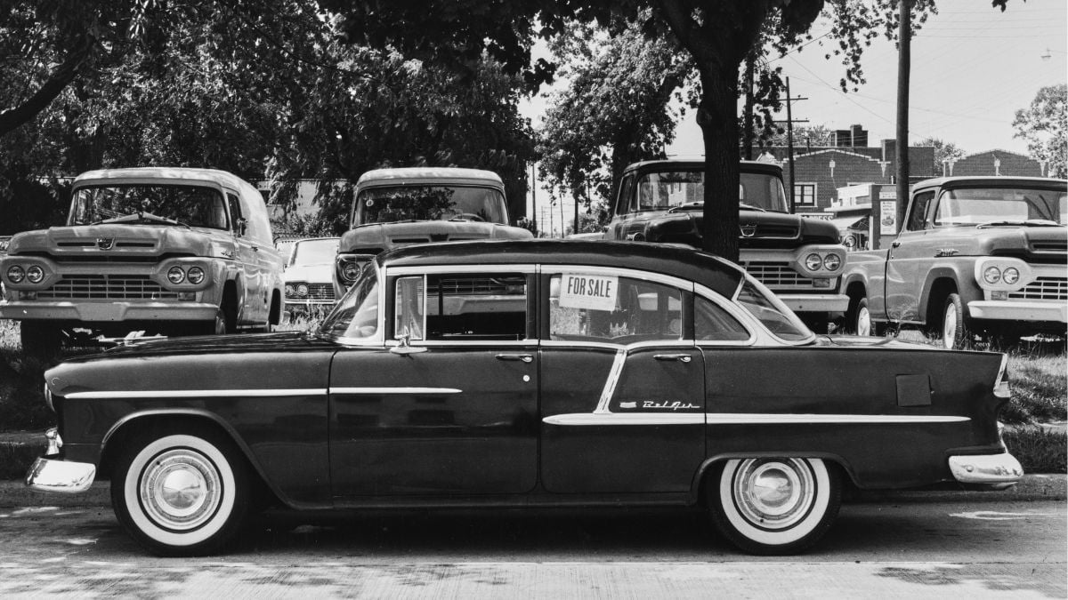 A vintage Chevrolet Bel Air with a “For Sale” sign in the window, parked in front of several other classic pickup trucks.