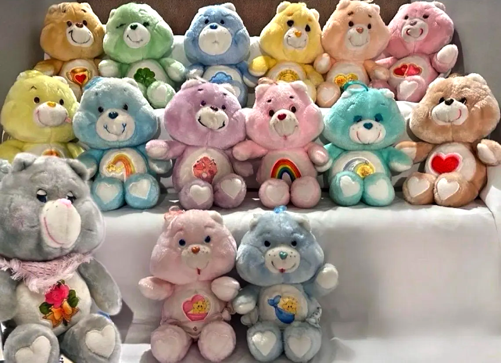 A collection of fifteen Care Bear plush toys in various pastel colors, each featuring a unique symbol on its belly.
