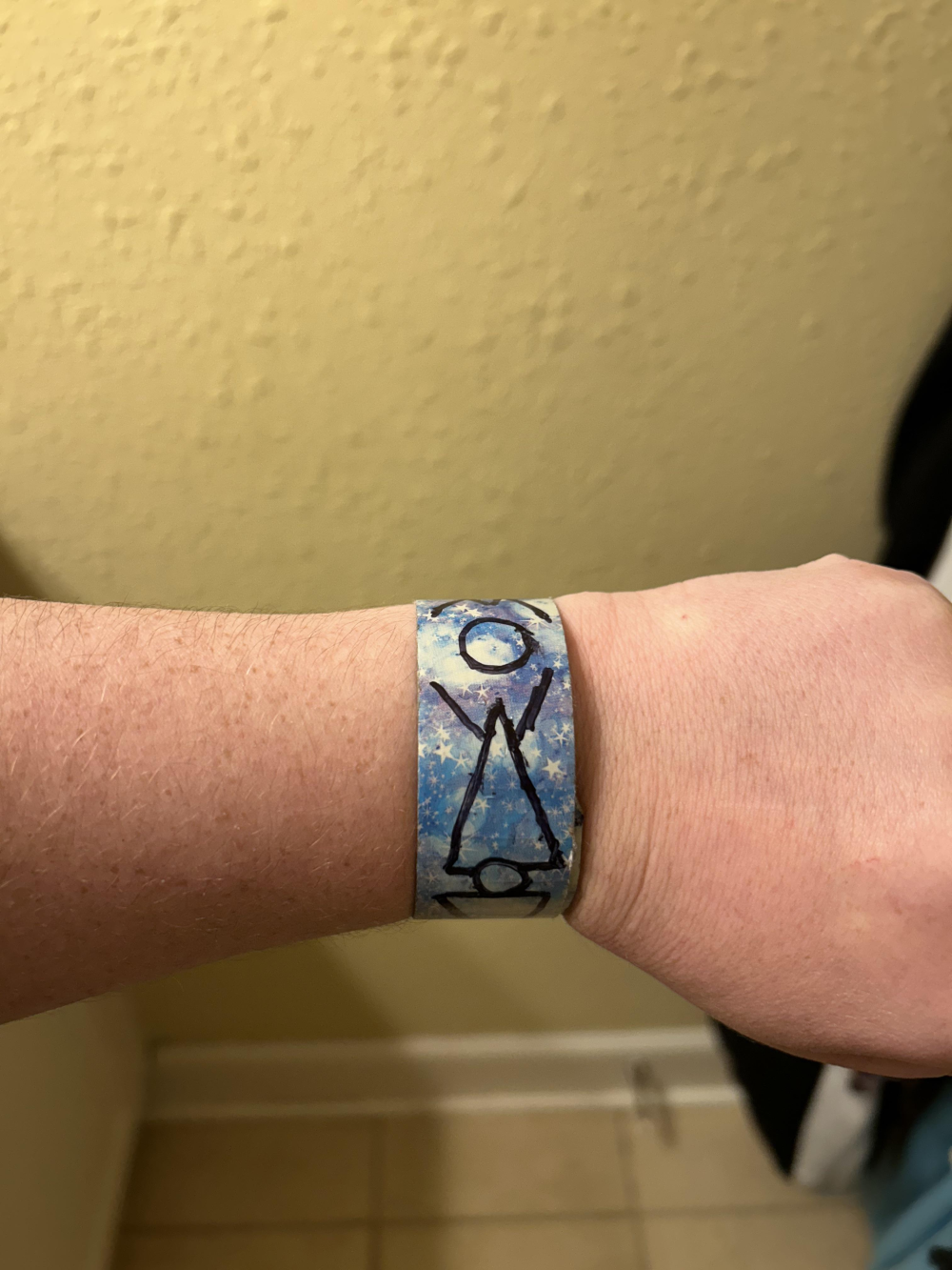 A blue star-patterned wristband with a hand-drawn black stick figure of a person inside a triangle.