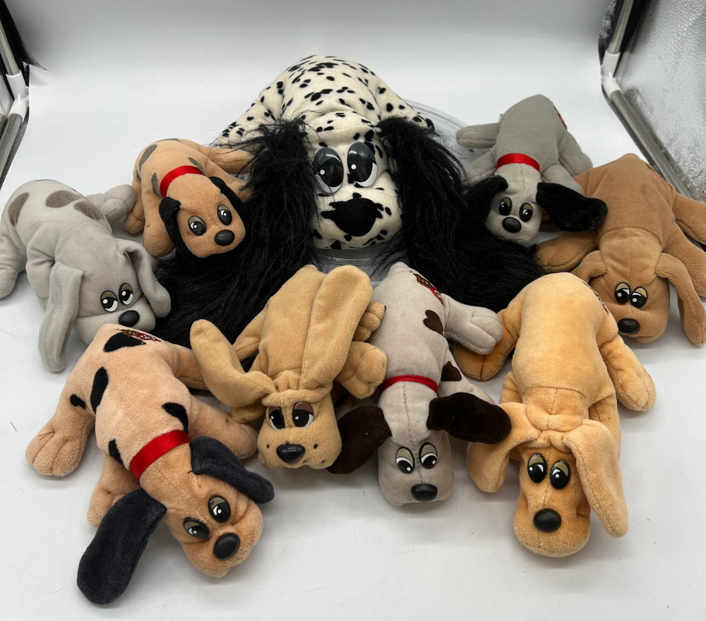 A group of ten plush toy dogs in various colors, including a large dalmatian in the center, arranged on a white surface.