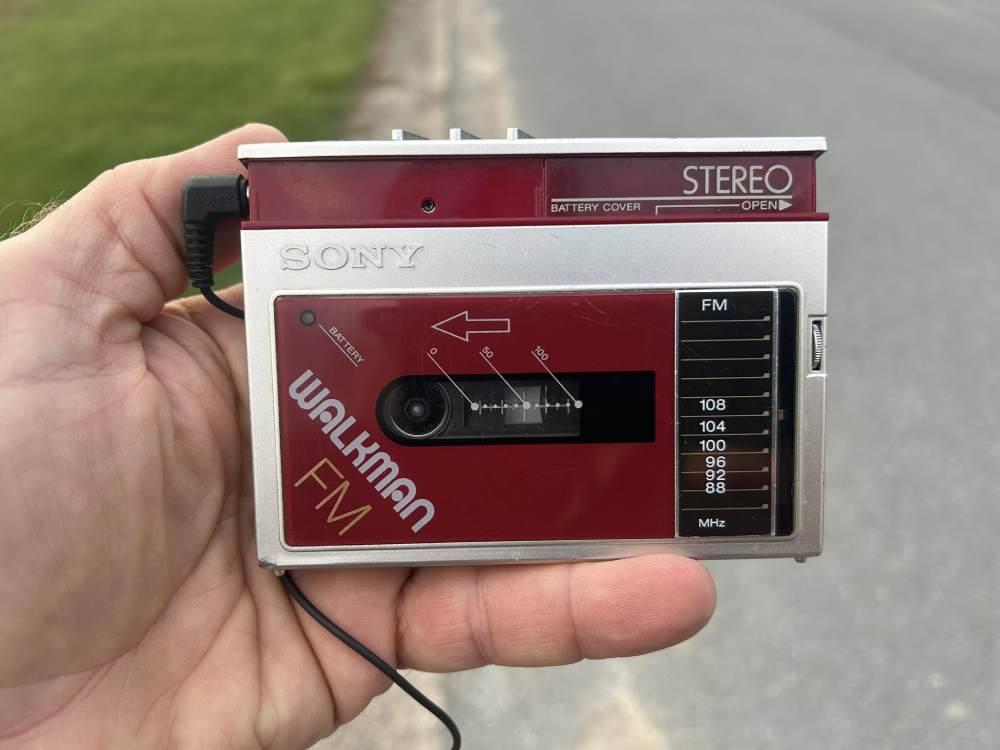 A hand holding a vintage silver and red Sony Walkman FM cassette player.