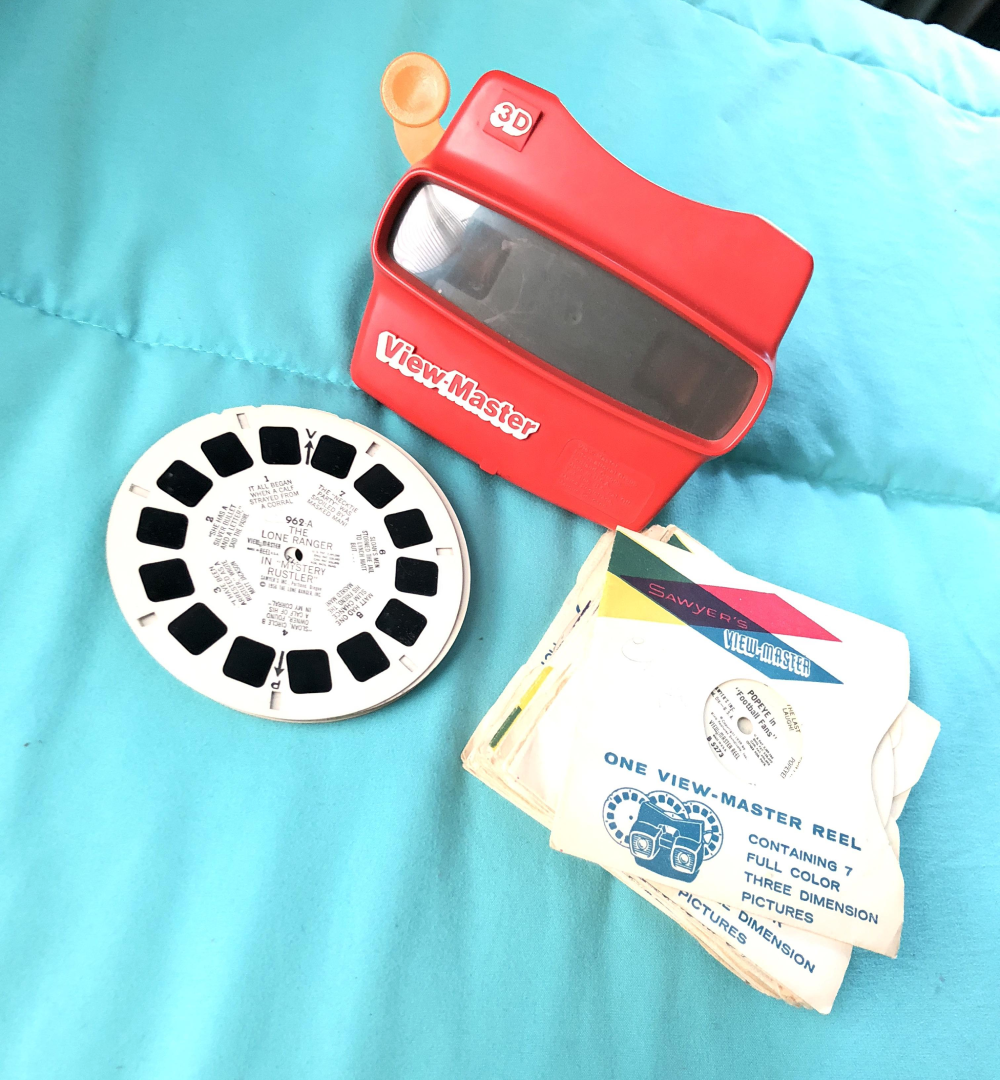 A red plastic View-Master toy, a Lone Ranger reel, and a stack of View-Master reel envelopes.