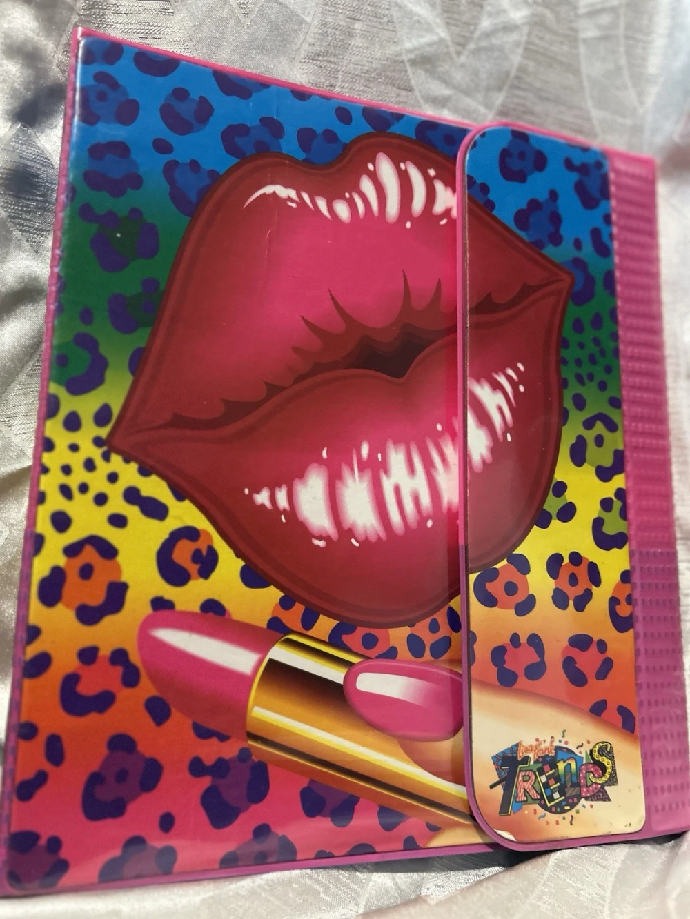 A colorful, leopard-print folder featuring a large illustration of glossy pink lips, a lipstick tube, and a “Trends” logo.