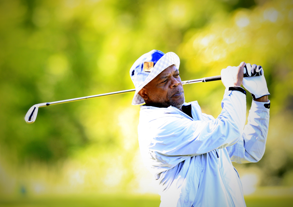 Samuel L. Jackson in a blue bucket hat swings a golf club.
