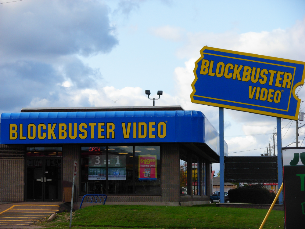 A Blockbuster Video store with a large blue and yellow roadside sign and storefront signage.