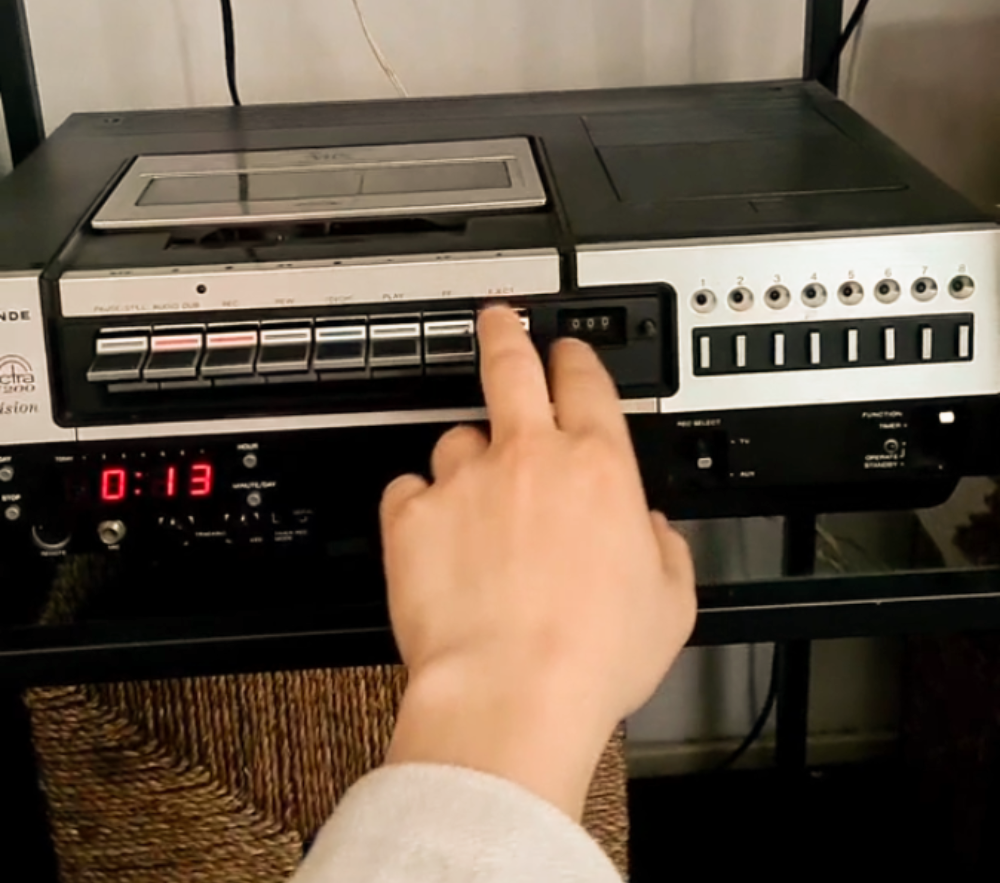 A hand pressing the eject button on a vintage VCR player.