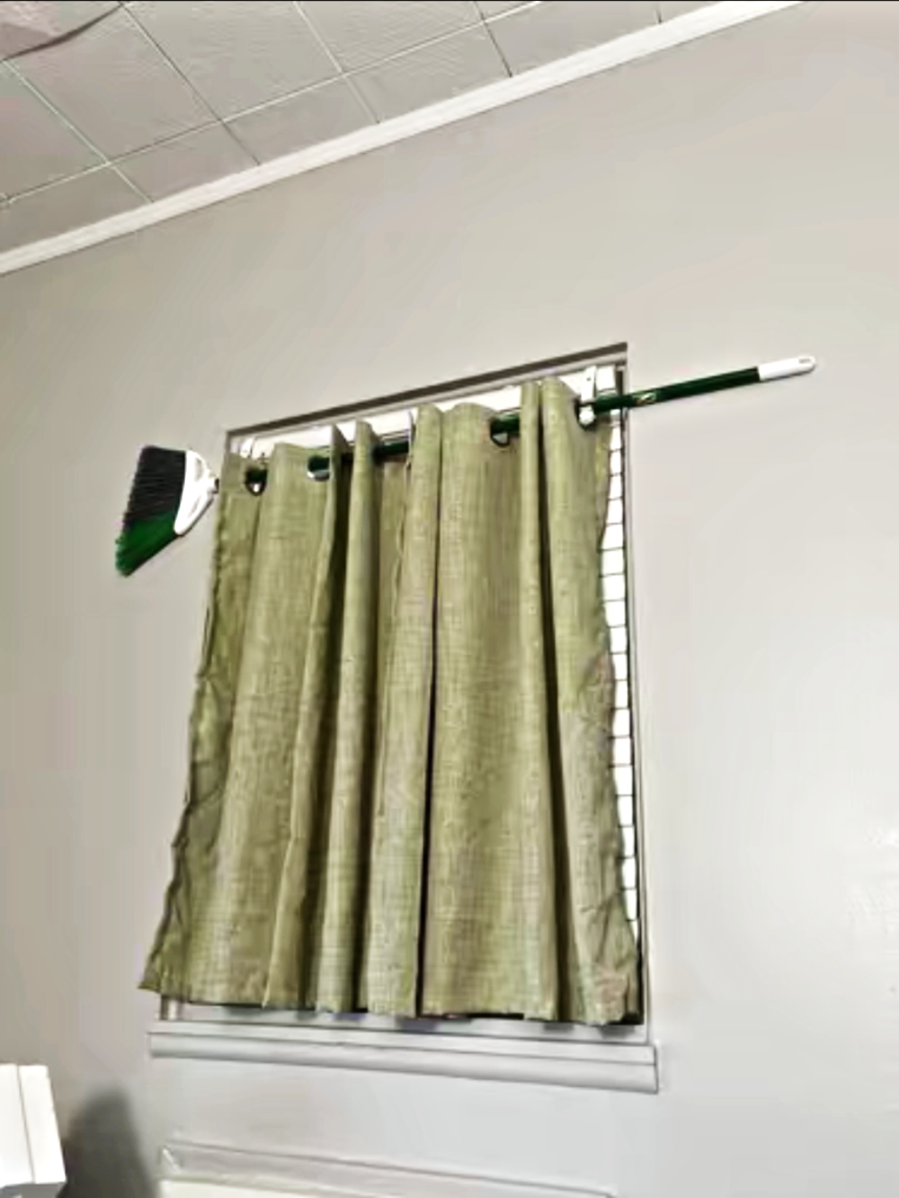 Green curtains hung on a broom handle acting as a makeshift curtain rod over a window.