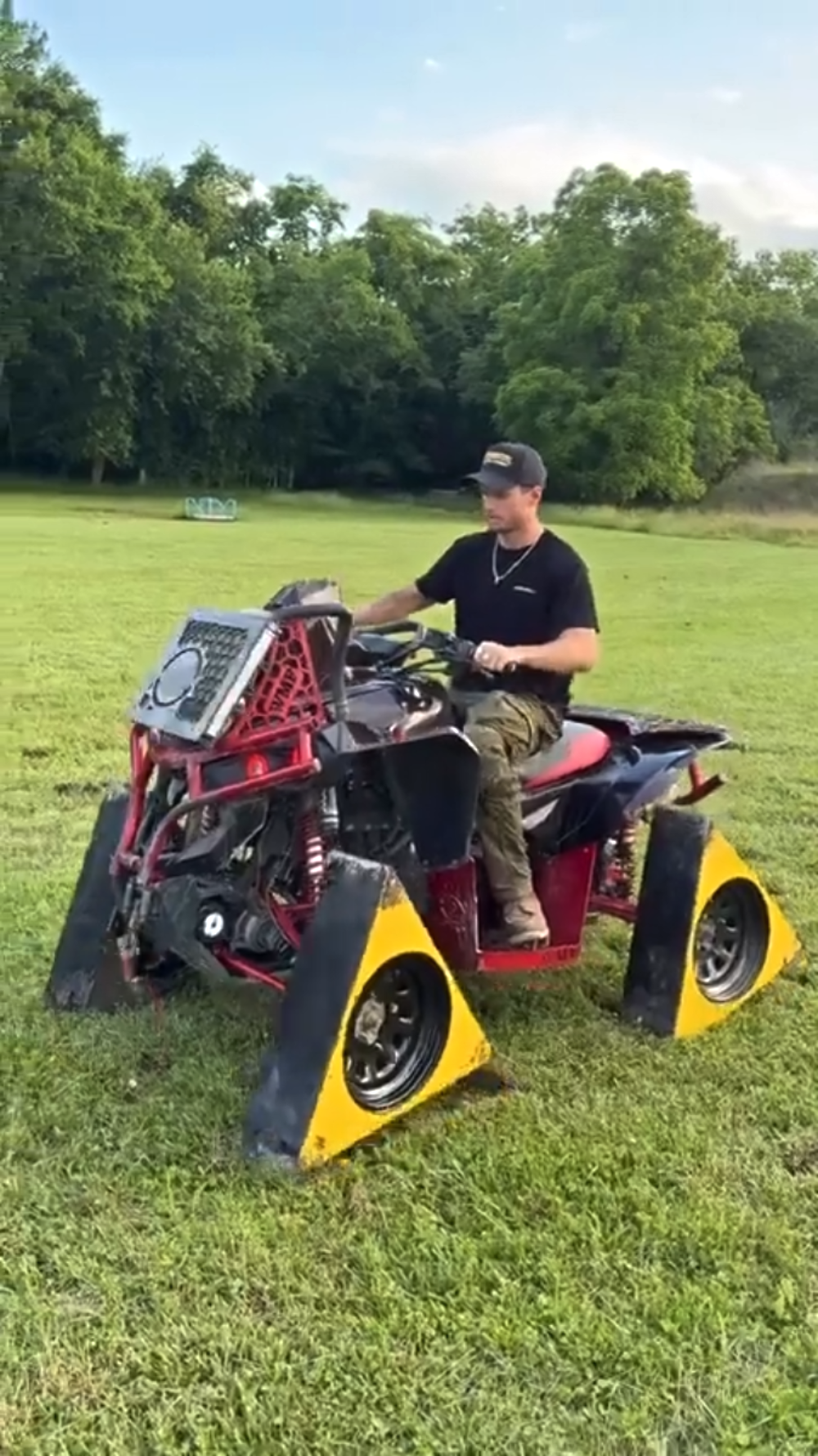 A man sits on an ATV fitted with large, triangular yellow wheels on a grassy field.
