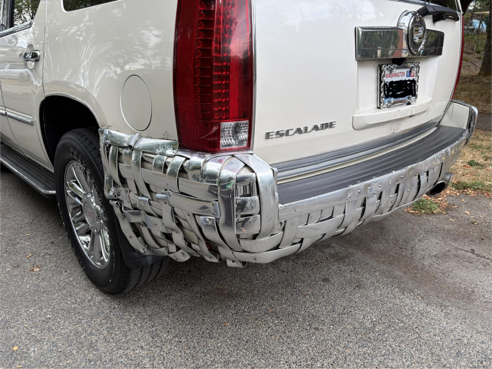 The rear bumper of a white Cadillac Escalade repaired with a basket-weave pattern of metal strips.