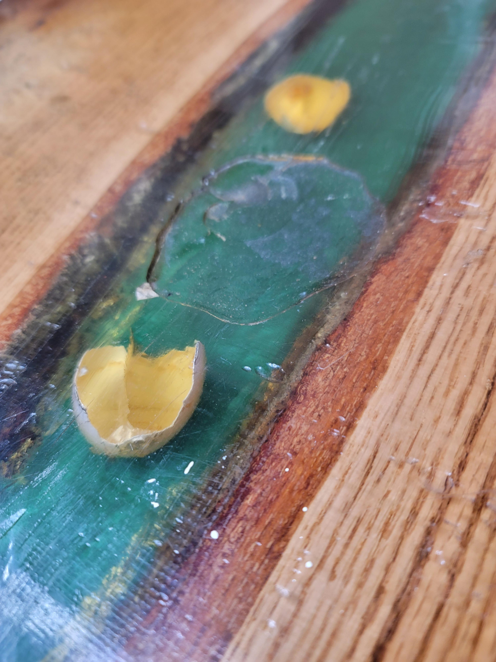 Two broken eggshell halves resting on a wooden table with a green resin inlay.