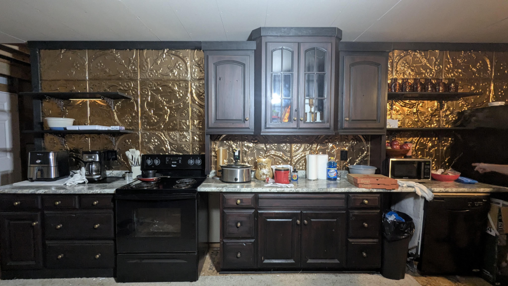Kitchen featuring dark wooden cabinets, a black stove, and gold-colored decorative metal backsplash tiles.