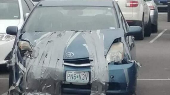 A blue Toyota sedan with its front bumper and hood held together by layers of gray duct tape.