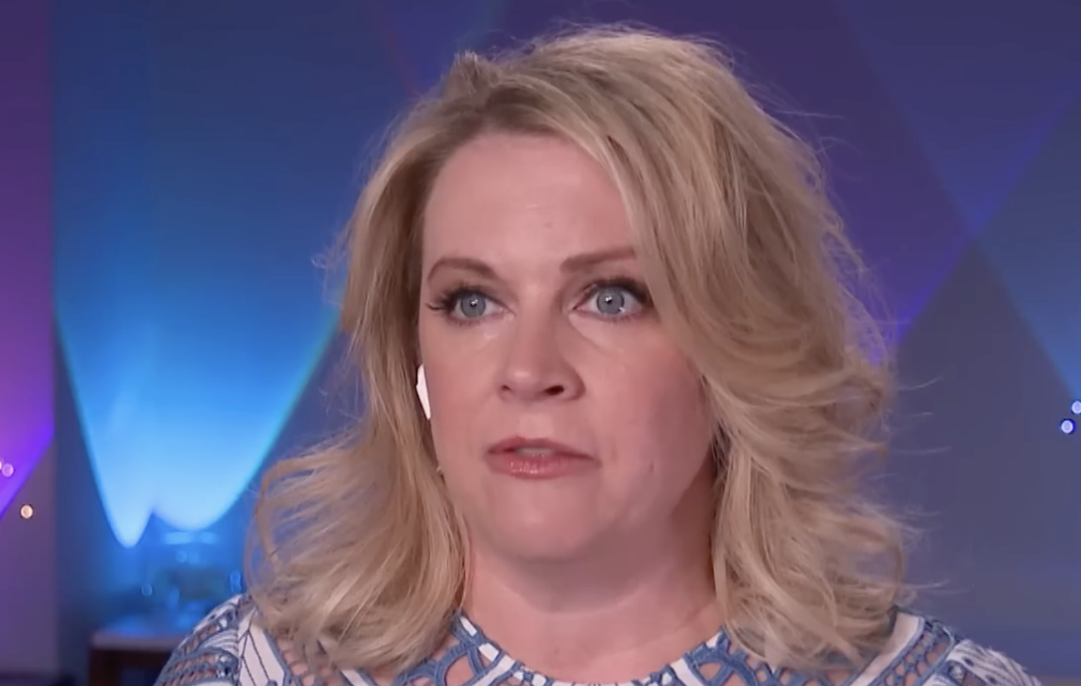 A blonde woman looking off-camera during a television interview.