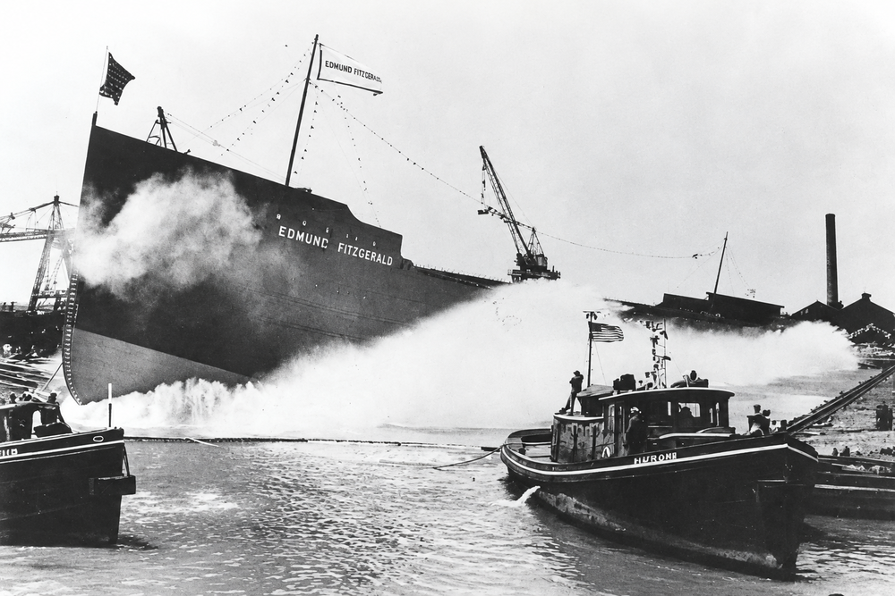 The freighter SS Edmund Fitzgerald sliding into the water during its launch, with tugboats nearby.