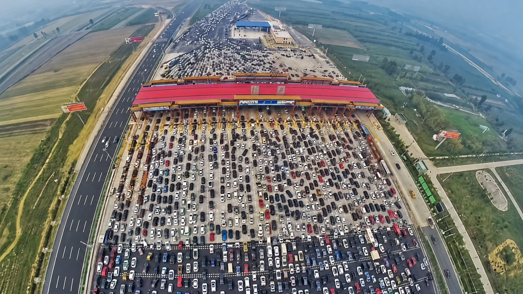 Aerial view of many cars backed up in lanes at a large highway toll plaza.