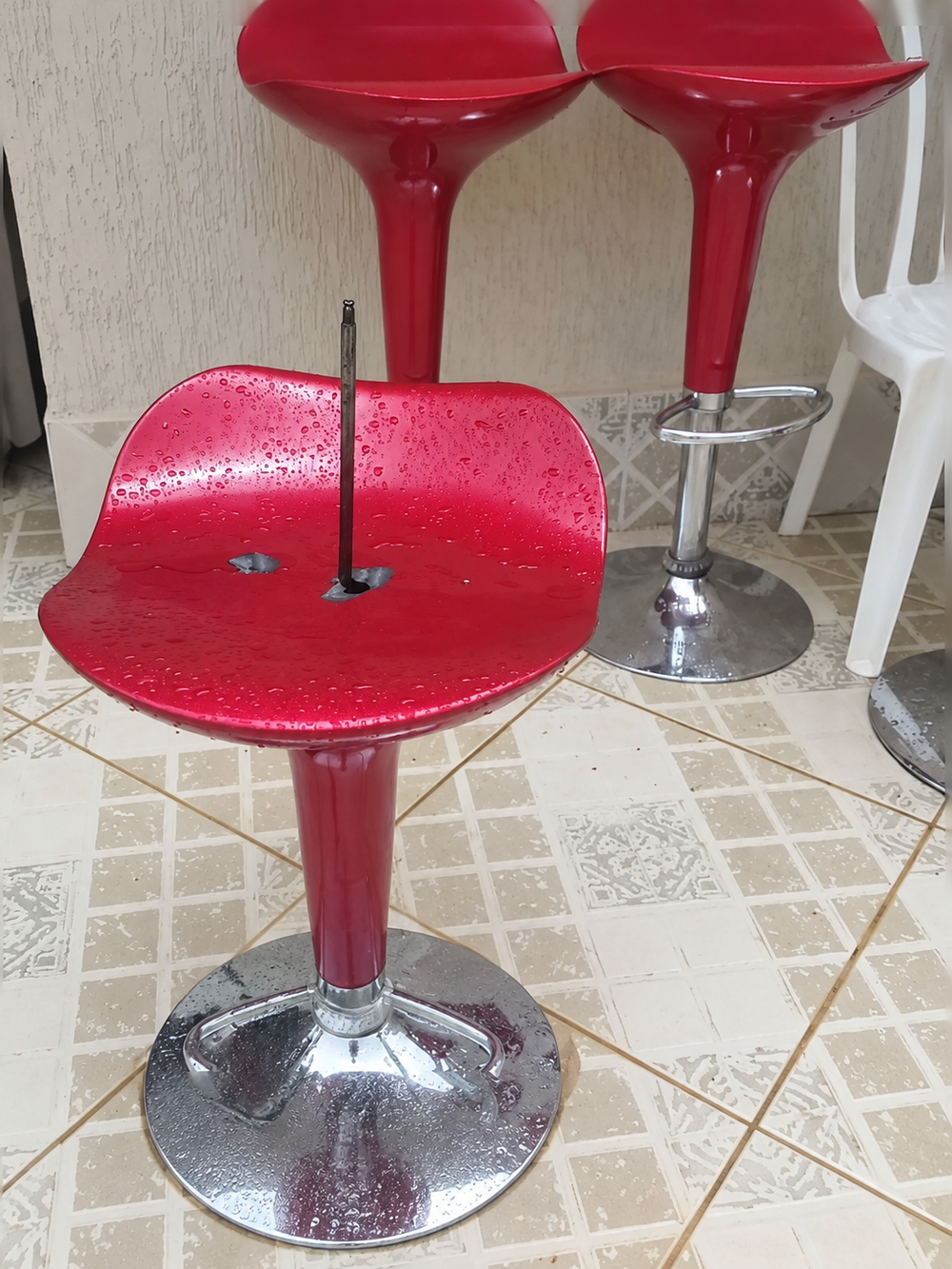 Three red bar stools on a tiled floor, with the seat of the front stool missing its backrest and showing a metal support post.