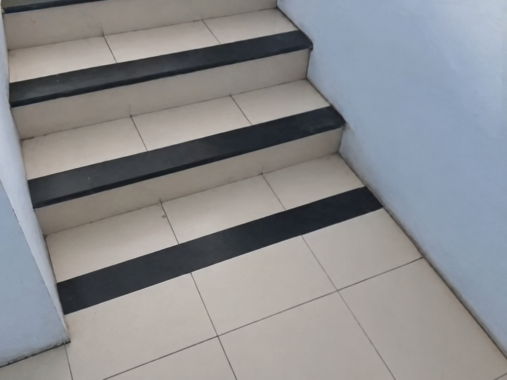 A short flight of stairs with white tile treads and black non-slip strips on each edge.